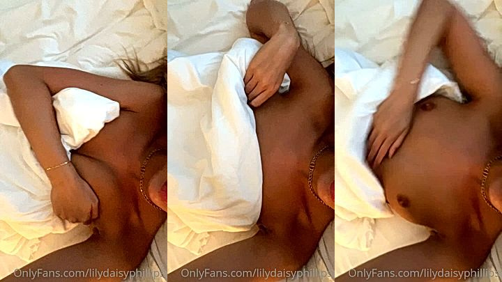 Lillian Phillips lying on the bed pulling down her cover to show her tits